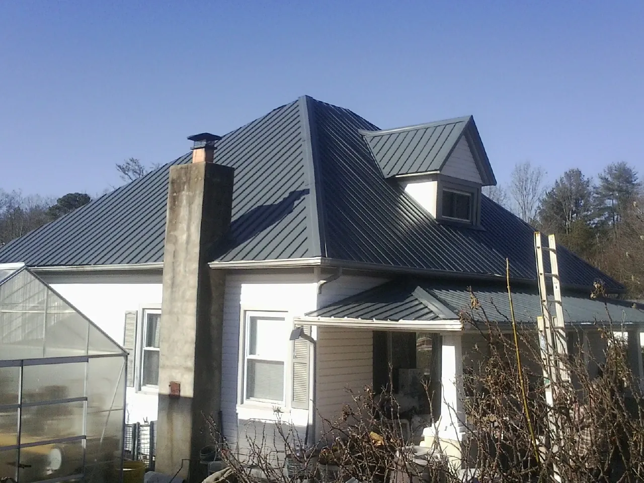 Dark blue standing seam metal roof on a white farmhouse with dormer — Slate & Tile Roof Repair by Roofing Brothers in Hemlock