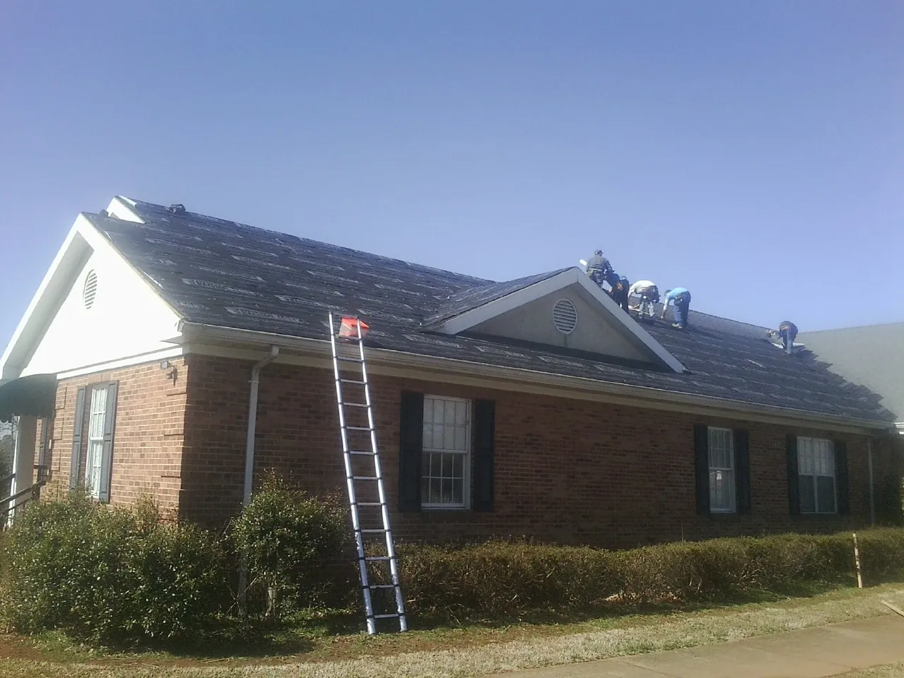 Crew tearing shingles off a brick ranch roof with a ladder set — Metal Roof Repair work by our crew in Hemlock