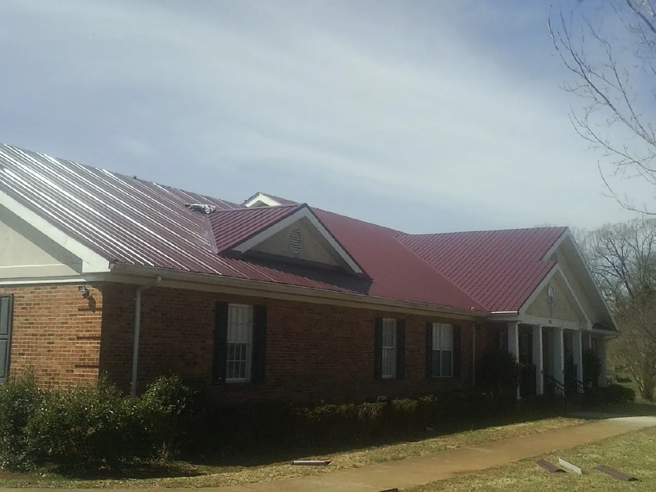 Red metal roof with gabled entries on a long brick building, from a Hail Damage Roof Repair job in Hemlock