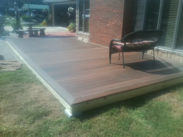 New wood deck and wicker chair beside a brick house in Hemlock