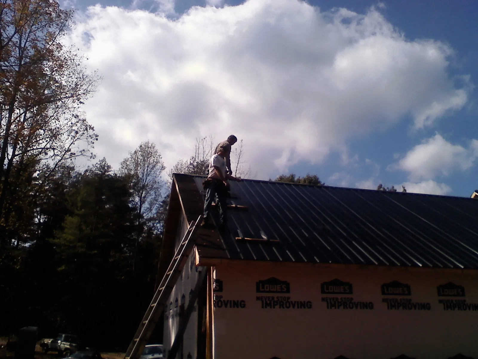 Roofer fastening dark metal panels high against a cloudy sky, from a Roof Inspection job in Hemlock