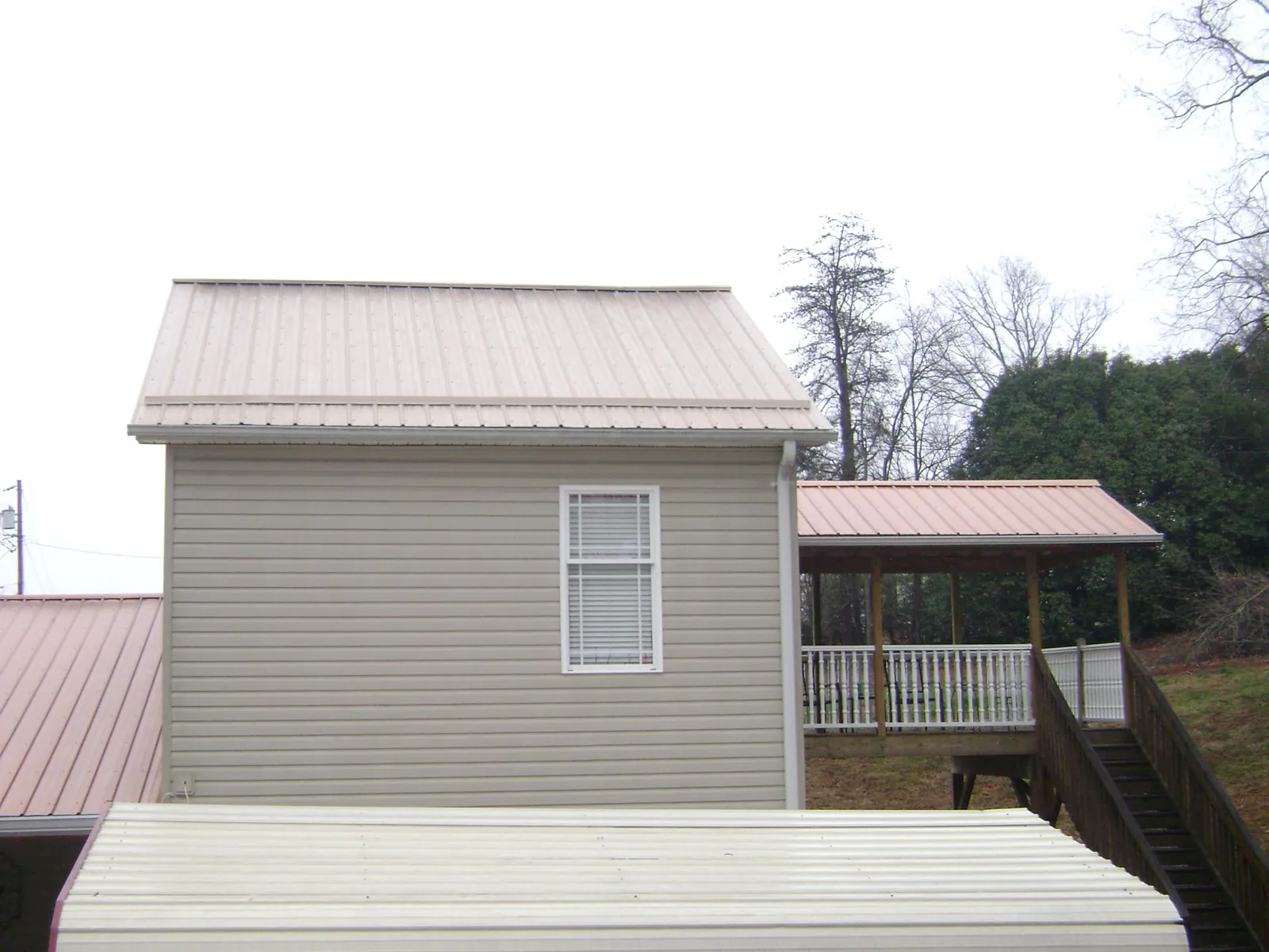 Tan metal roofs on a two story addition and attached porch, from a Roof Replacement job in Hemlock